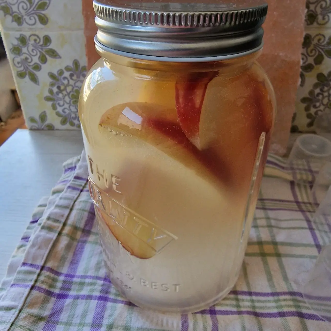 Ein Glas mit frisch angesetzter wilder Hefe und Apfelstücken auf einem Küchentuch, bereit für die natürliche Fermentation.